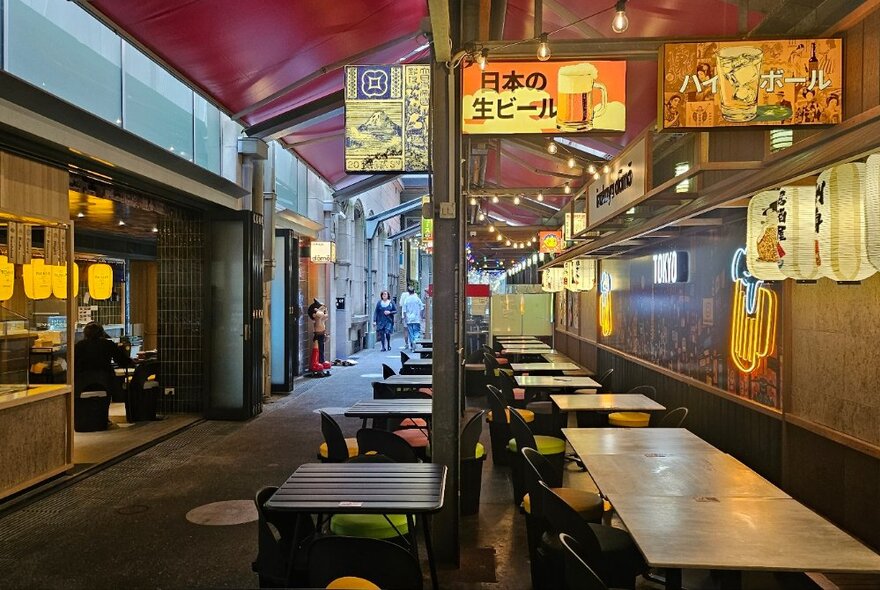 Laneway izakaya bar with outdoor tables and chairs, long dining tables and illuminated signs. 