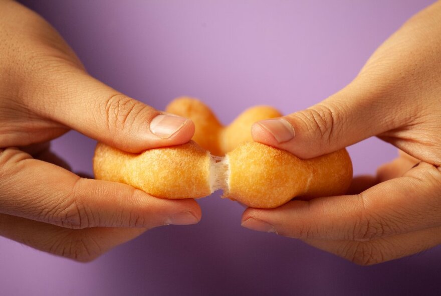 Hands breaking open a round ring of donuts.