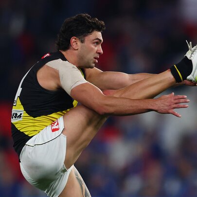 Side profile of a Richmond AFL player with his leg raised very high in front of him, having just kicked a football.