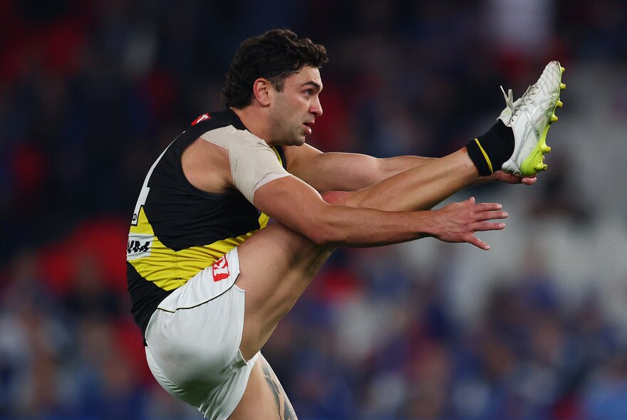 Side profile of a Richmond AFL player with his leg raised very high in front of him, having just kicked a football.