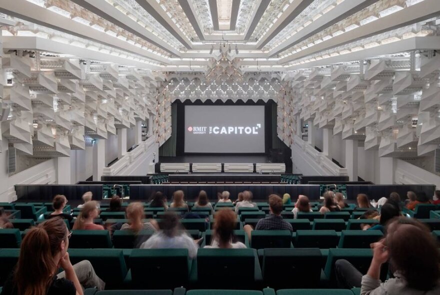 People seated in rows in the art deco cinema The Capitol looking at an empty screen waiting for a film to start.