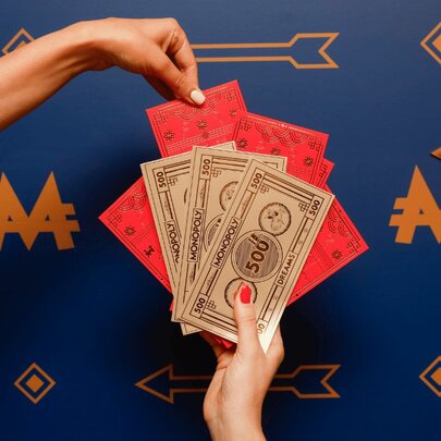 Two hands holding Lunar New Year themed Monopoly cash and red envelopes.