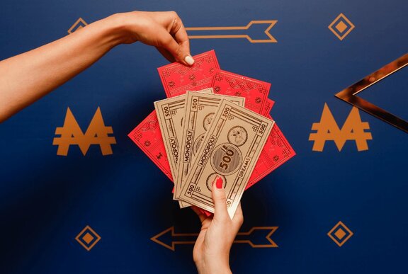 Two hands holding Lunar New Year themed Monopoly cash and red envelopes.