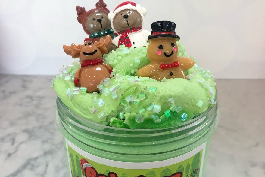 A jar of green slime, with small Christmas themed toys wedged in the top of the slime.