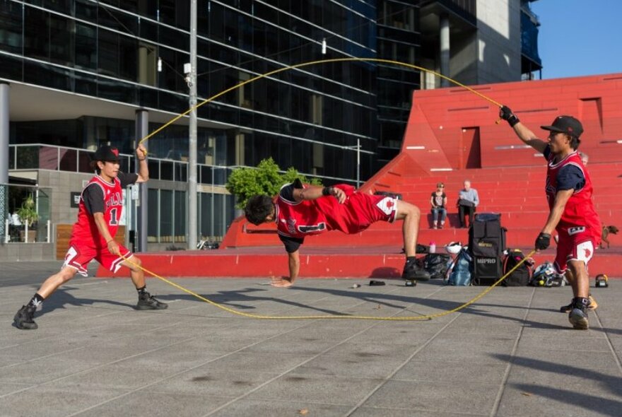 Street performers doing acrobatics with skipping ropes in front of a red amphitheatre