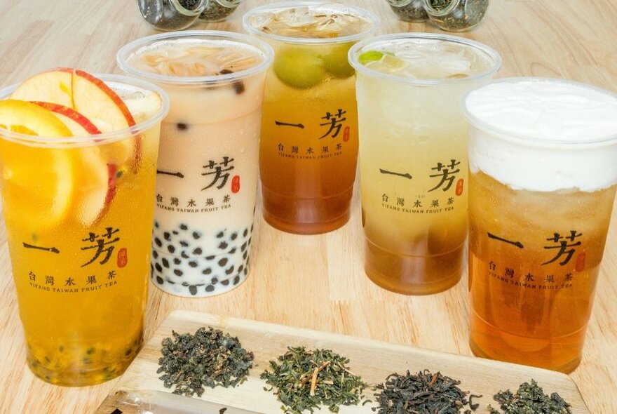 Five different fruit teas on display on a wooden counter, some with a fruit garnish.