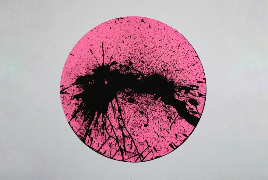 A print showing a central pink circle with paint black splatters, against a grey background. 