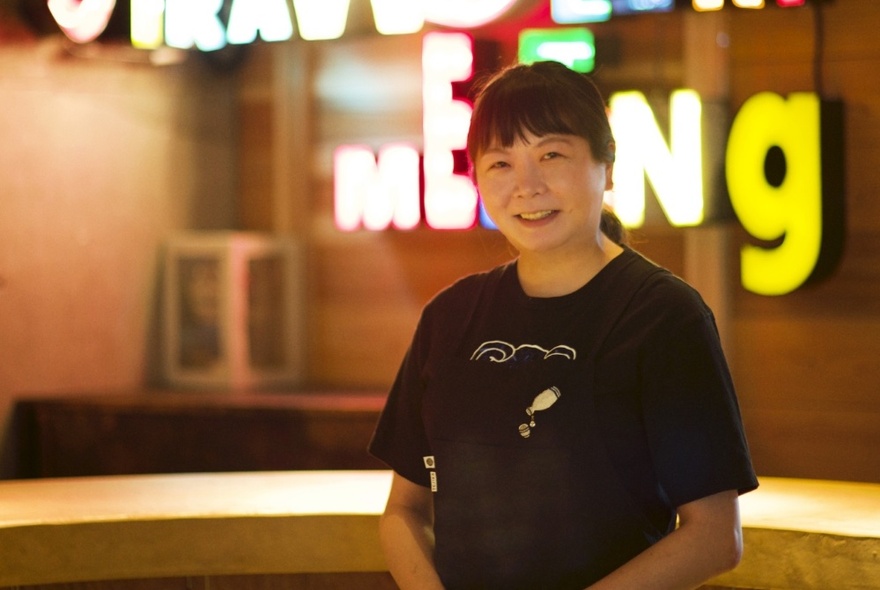 Sake samurai Marie Chiba standing in front of illuminated lettering and smiling. 