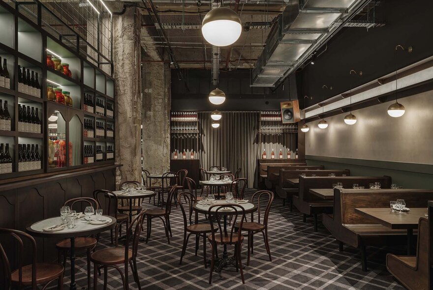 An industrial style restaurant with wine bottles on the wall and timber chairs. 