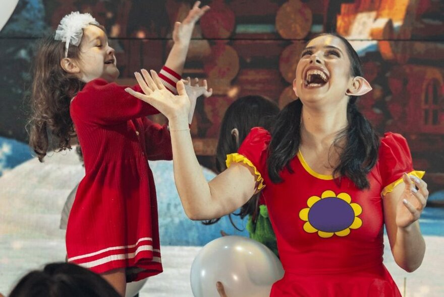 A lively moment from a holiday-themed family experience featuring a festive elf in costume and a young child throwing white balloons in the air. 