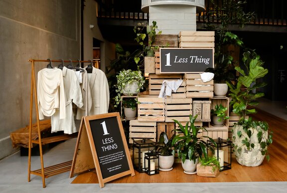 A pile of wooden crates with clothing in them next to clothes racks and a blackboard stand.