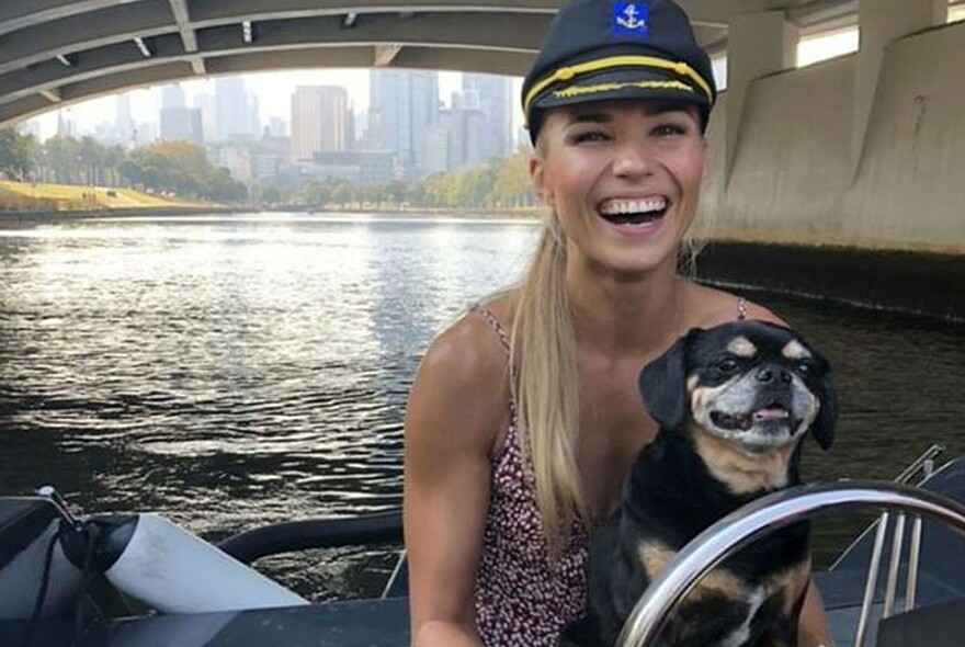 Woman and a dog having fun driving a small boat along the Yarra River.