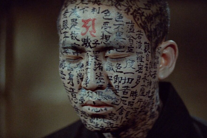 A still from a J-Horror movie of a Japanese man's heavily tattooed face and head.