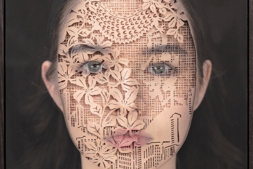 Photograph of a face superimposed with a delicate cut-out stencil pattern of foliage against a grid background.