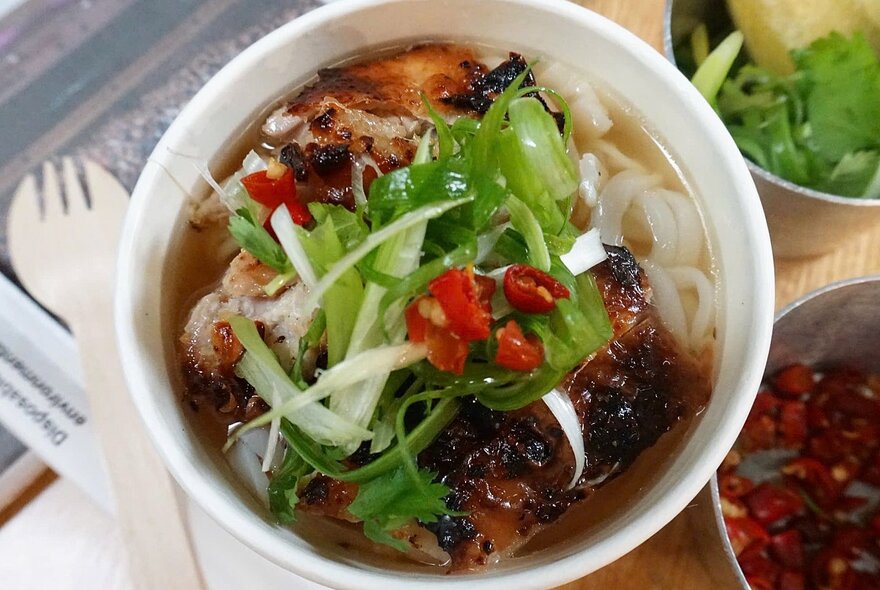 Cup of Asian soup with noodles and garnishes.