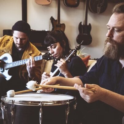 A Persian percussionist playing a drum, two musicians playing guitar and lute behind him.
