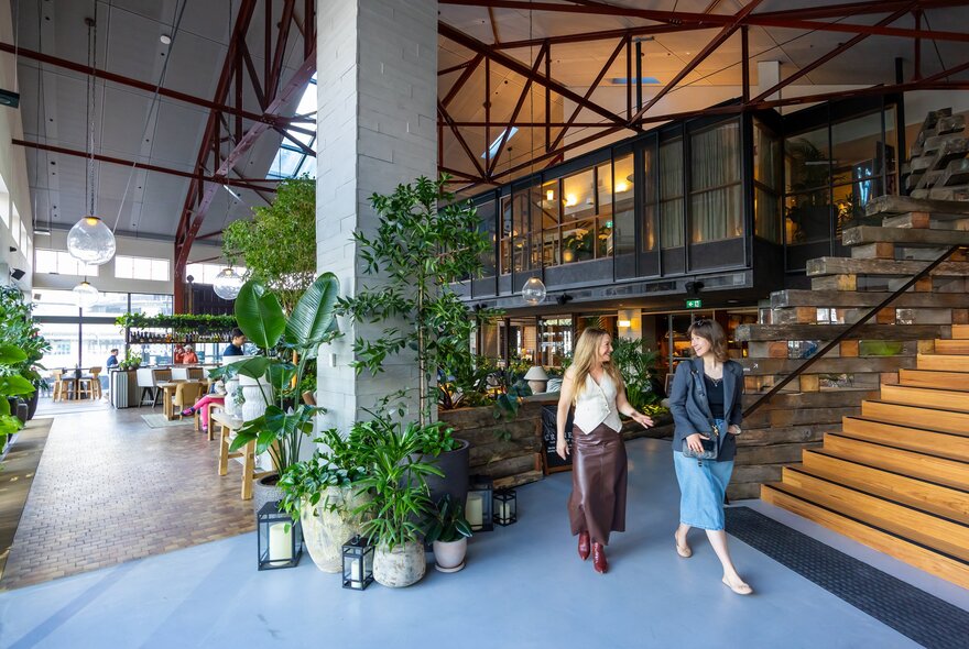 Two friends are walking through a hotel lobby surrounded by lush plants