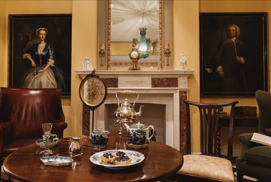 Morning room dressed in 18th-century antiques including fireplace and mirror, breakfast table and paintings.