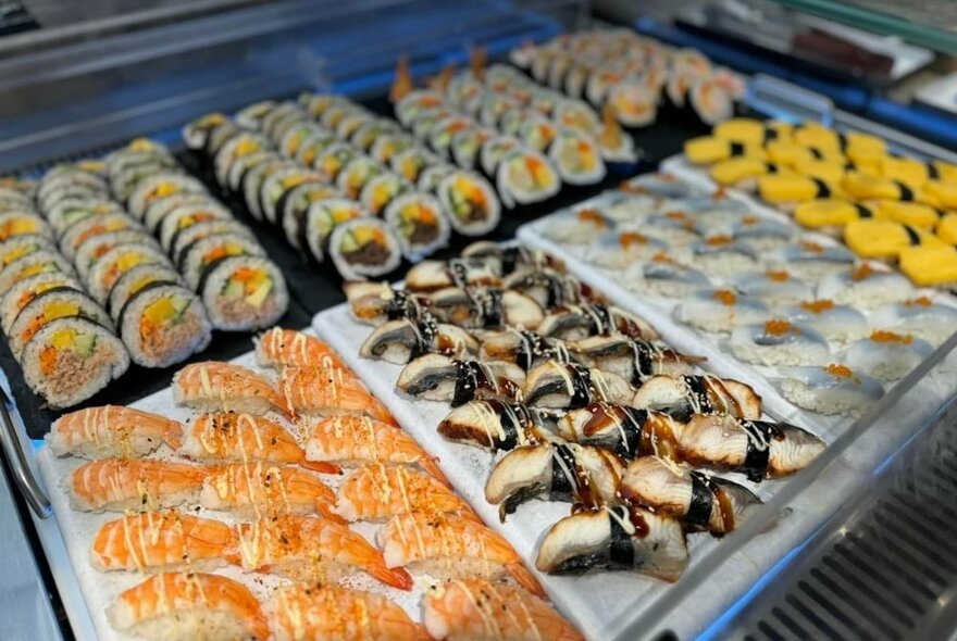 Trays of sushi including salmon and egg rolls.