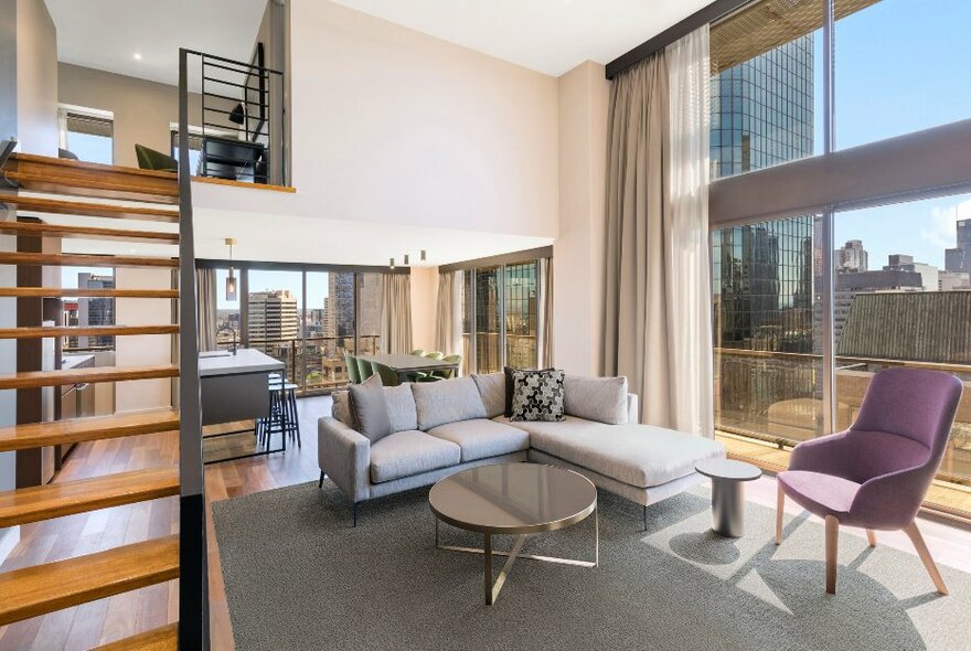 Hotel apartment with downstairs lounge and kitchen, wooden steps leading up to mezzanine bedroom.