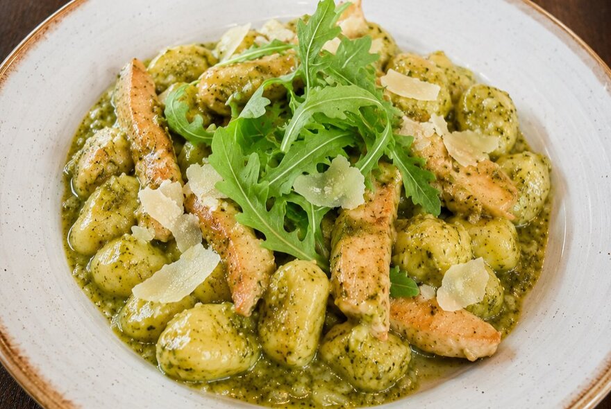 A bowl of pesto gnocchi with rocket garnish. 