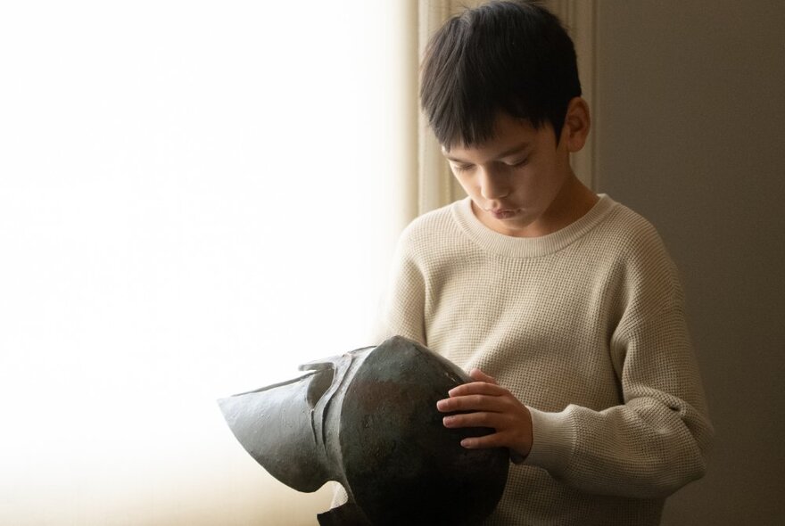A child looking at a replica of an Ancient Greek helmet.
