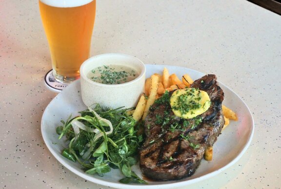 A steak, fries and salad on a plate, with a schooner of beer behind it.