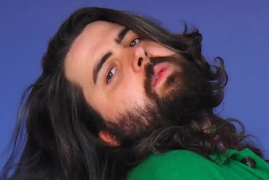Man with long dark hair and beard, stretching his head back to the side.