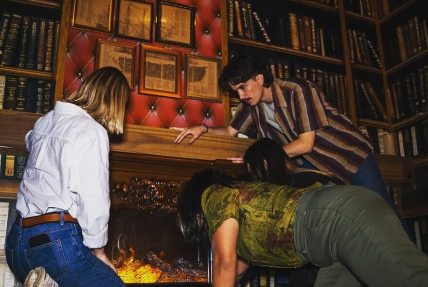  A group peering into a fireplace in a room decorated like a library with shelves of books.