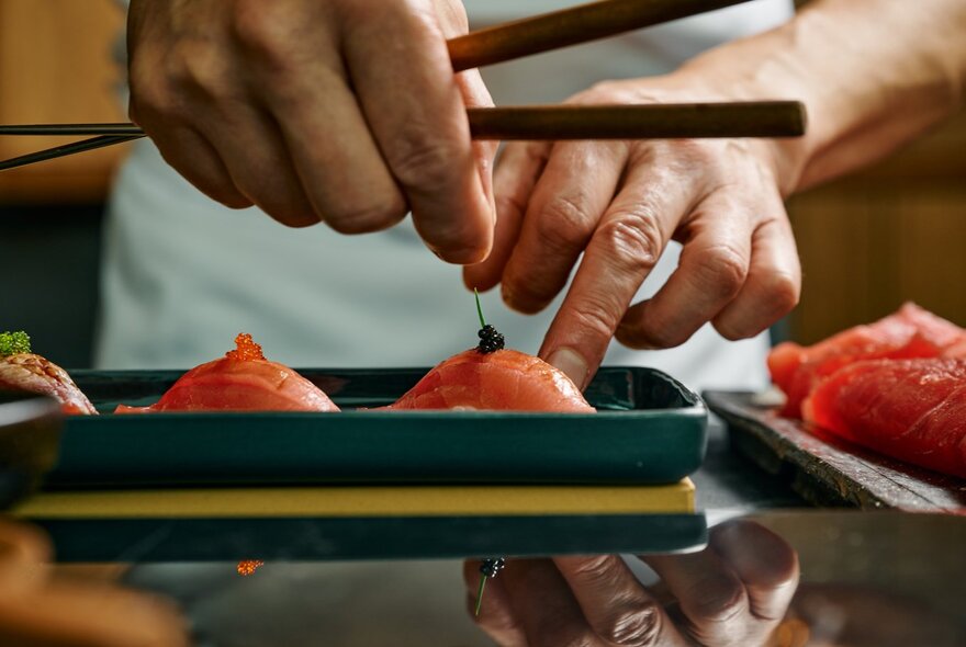 A chef carefully placing a tiny garnish on a salmon sushi platter.