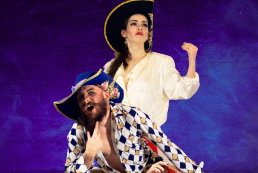 Two stage performers in colourful pirate costumes against a purple-blue background.