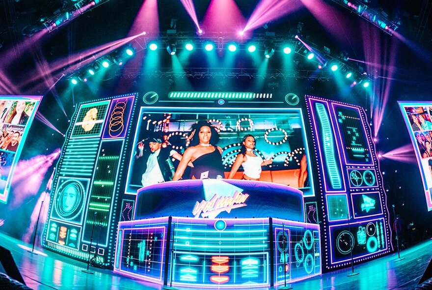 Video screen effect on a stage lit with purple and blue lights.