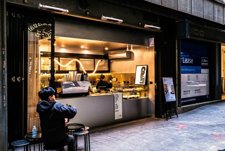 A laneway coffee window with stools outside and a wavy neon light.