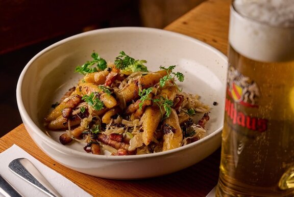 German potato dumpling, served with sauerkraut and speck, with a glass of beer next to it.