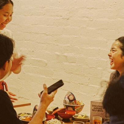 Waitress serving two diners in a Japanese cafe with painted white brick walls.