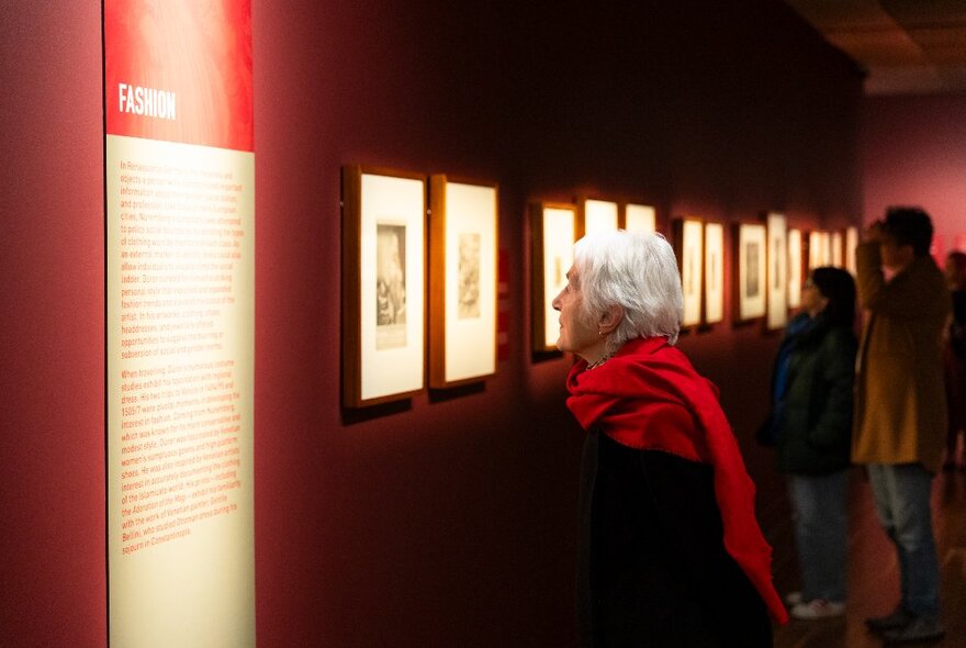 People in a dimly lit gallery looking at a display of framed prints and information.