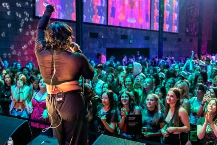 Performer with microphone on a stage in front of a crowd of young people.