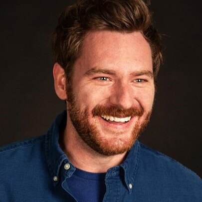 Portrait of comedian Cameron James smiling, wearing a blue shirt.