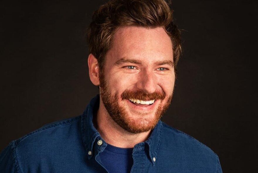 Portrait of comedian Cameron James smiling, wearing a blue shirt.