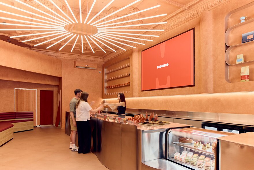 A couple being served in an ice cream shop with warm lighting and a large light installation.