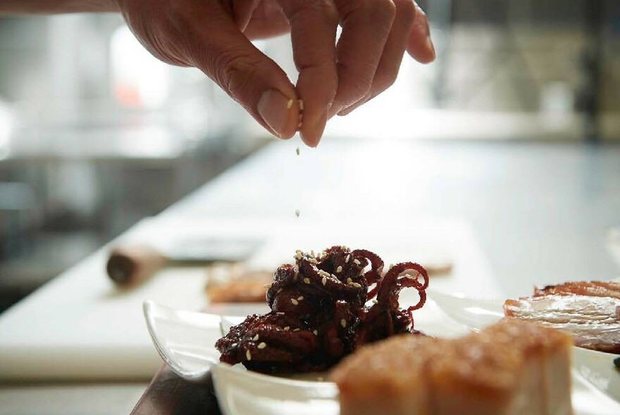 Someone sprinkling sesame seeds on top of a dish.