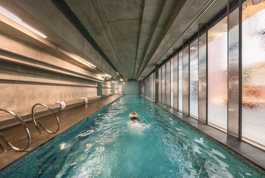 A very long hotel lap pool with marble surrounds and single swimmer in the lane. 