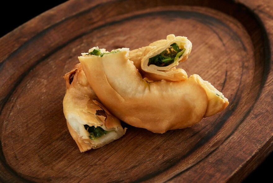 Wooden board with spring onion pancake sliced in half.