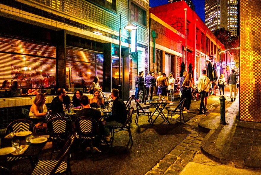 A bar exterior at night with coloured lights and people dining outside.