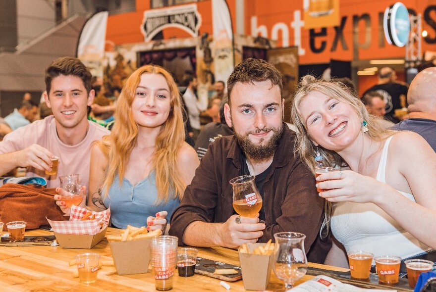 Two couples with beer and hot chips, seated at a bar table in an expo venue.