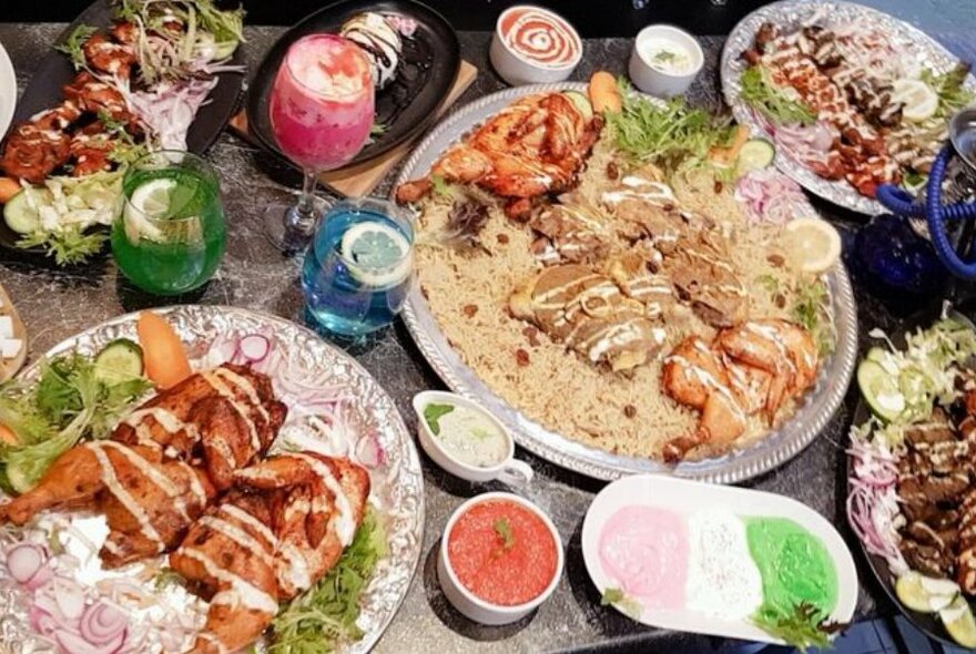 A table laden with many plates and bowls of Arabian food and colourful drinks.