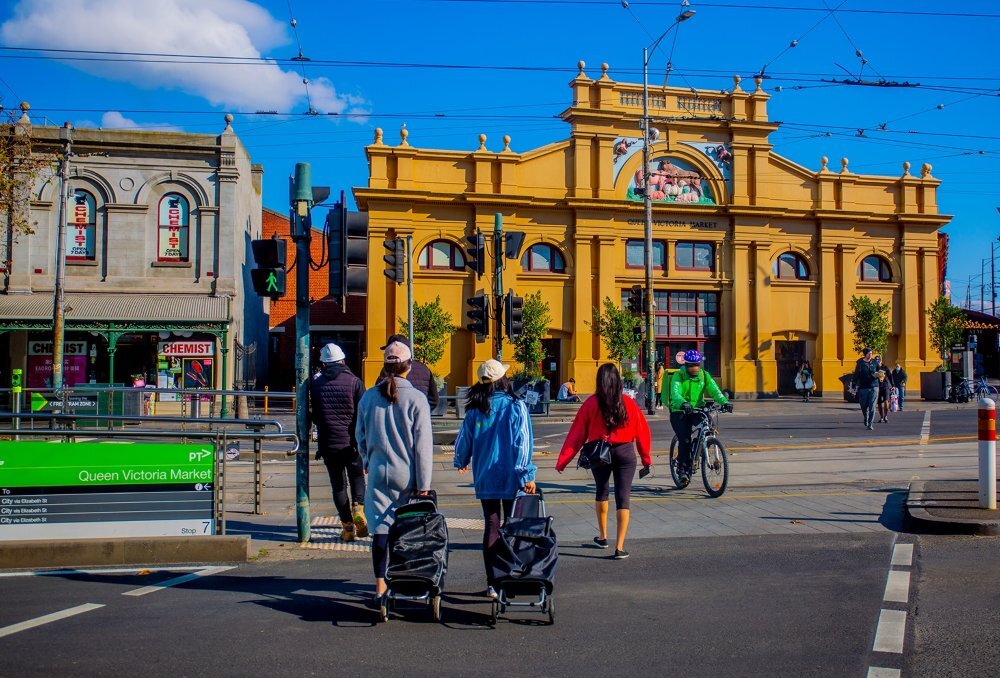 People are walking into a market with trolleys. 