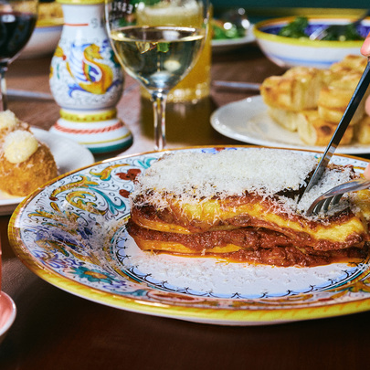 A person is cutting into a slice of lasagne on a colourful plate