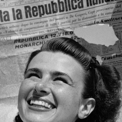 A black and white image of a woman from the 40s with a beaming smile in front of an Italian newspaper. 