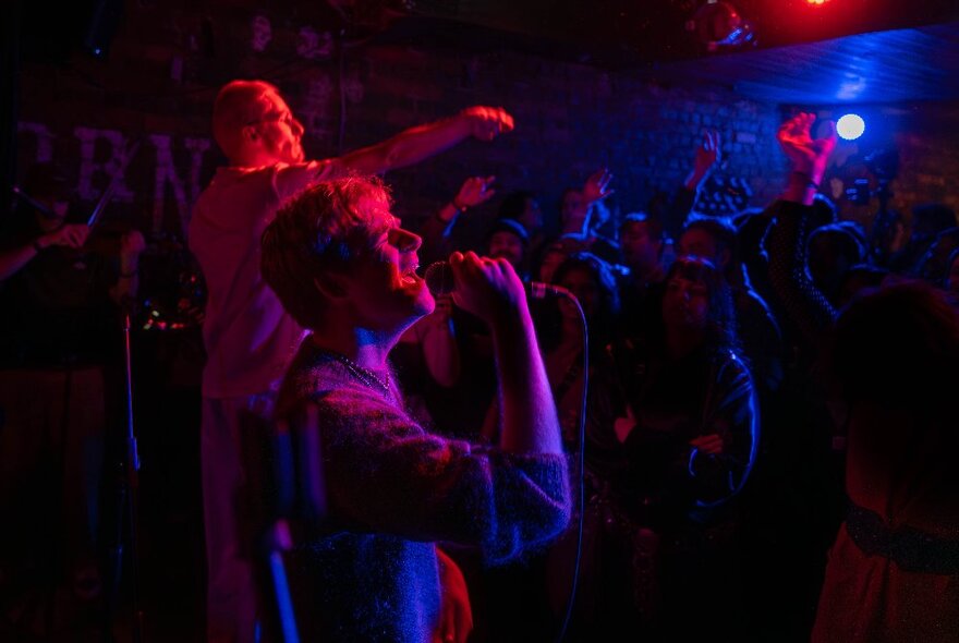 Singers performing with microphones under blue and red lights in a dark club.